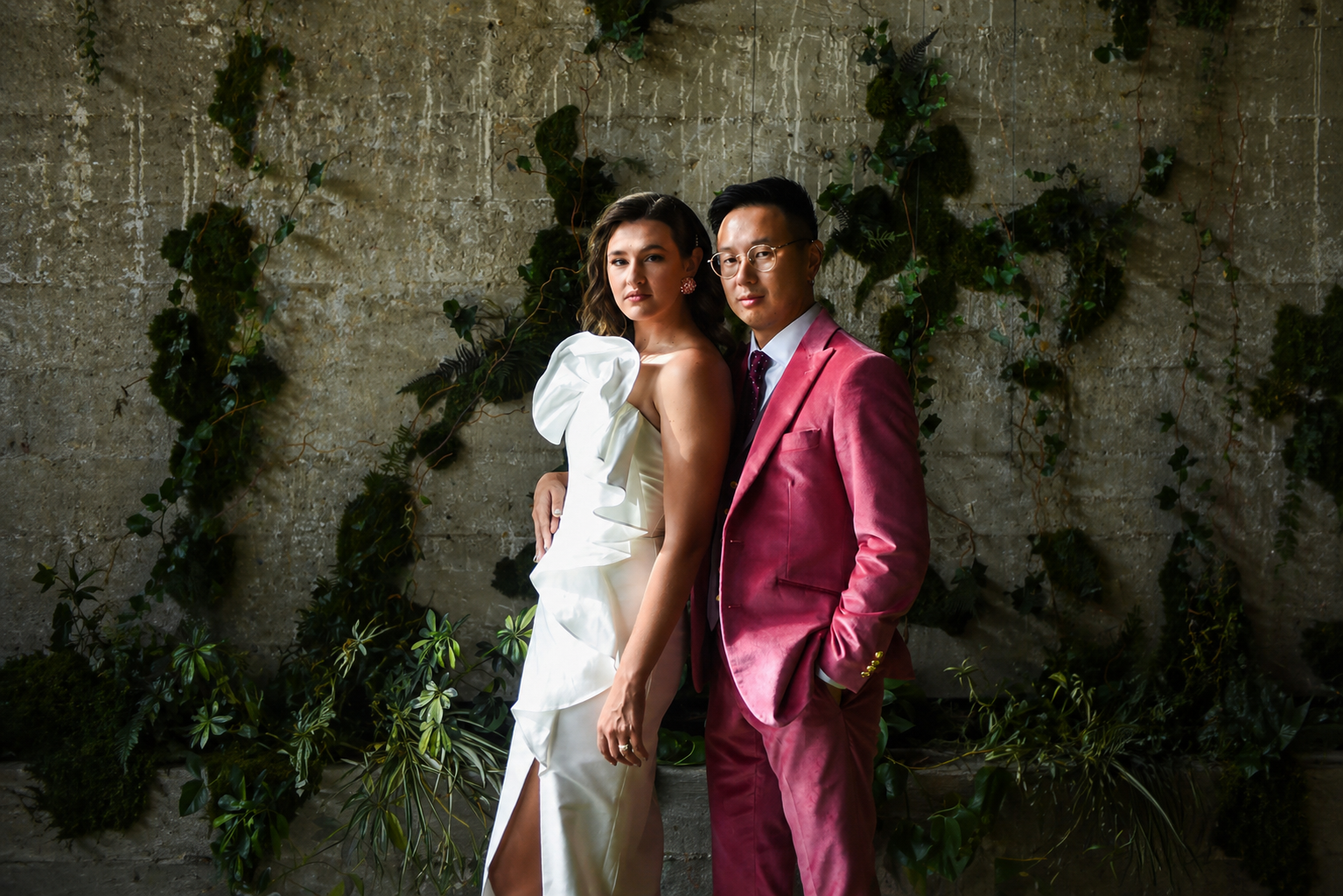 Bride and groom posed against a moss-covered concrete wall